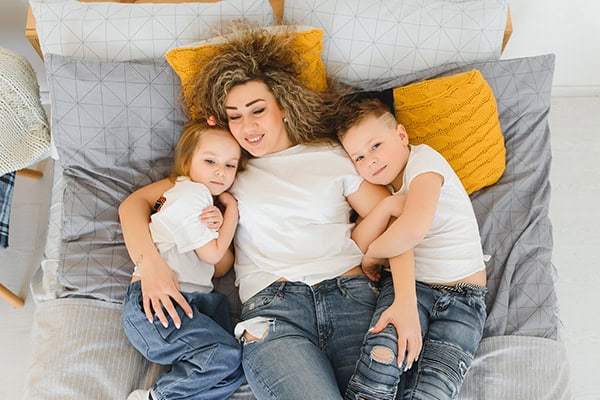 Happy mother with two children lying on bed, family moments, cozy home scene.