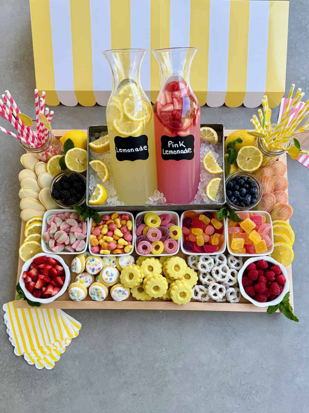 Colorful lemonade drinks with lemon slices and assorted candies on a tray.