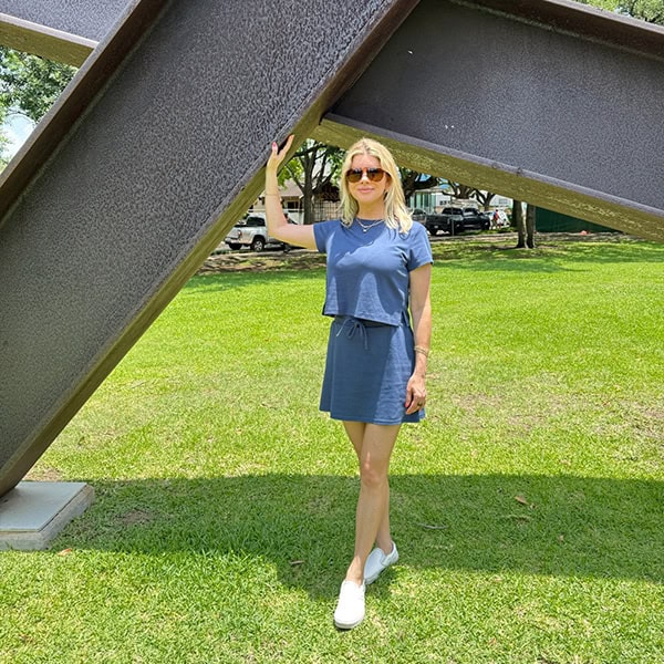 A woman in a blue dress and sunglasses standing outdoors under a large metal sculpture in Ocean City.