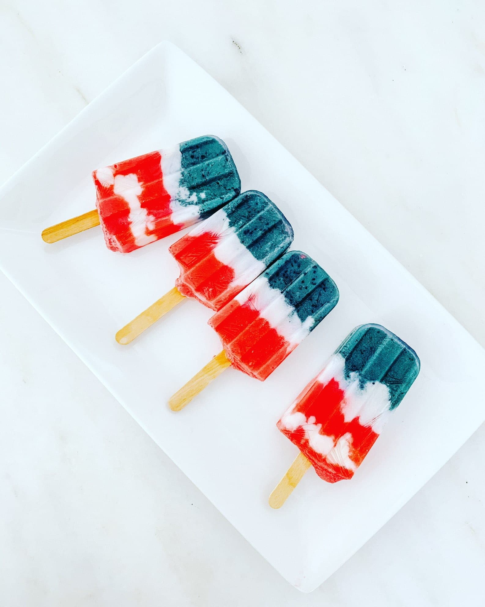 Colorful patriotic popsicles with red, white, and blue stripes on a white plate.