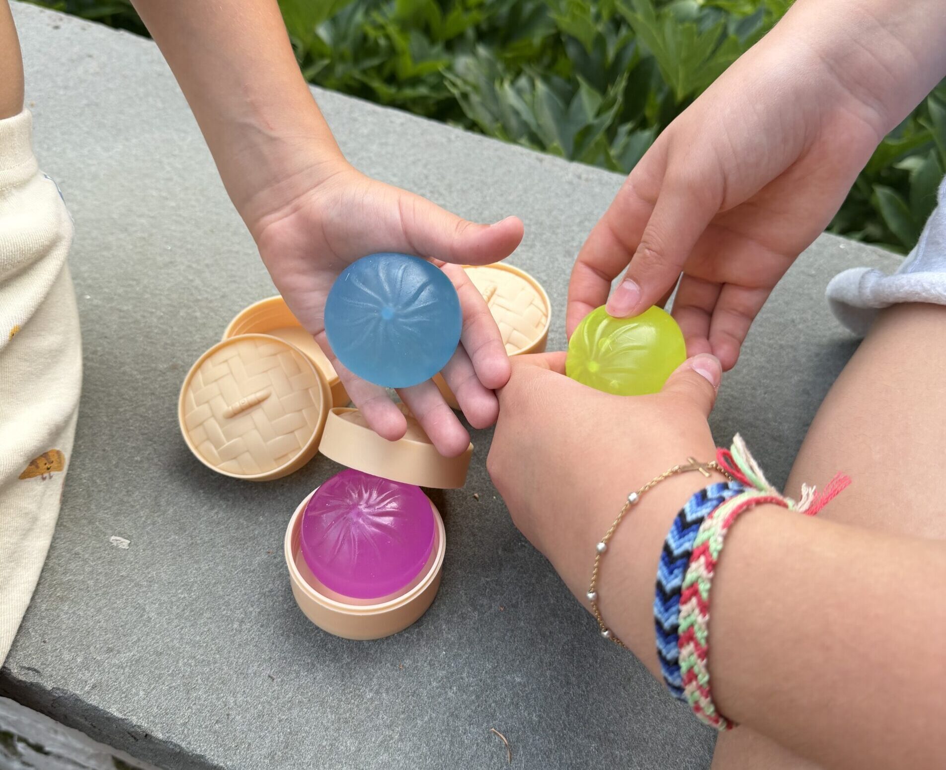 Children playing with colorful plastic containers outdoors on a concrete surface.